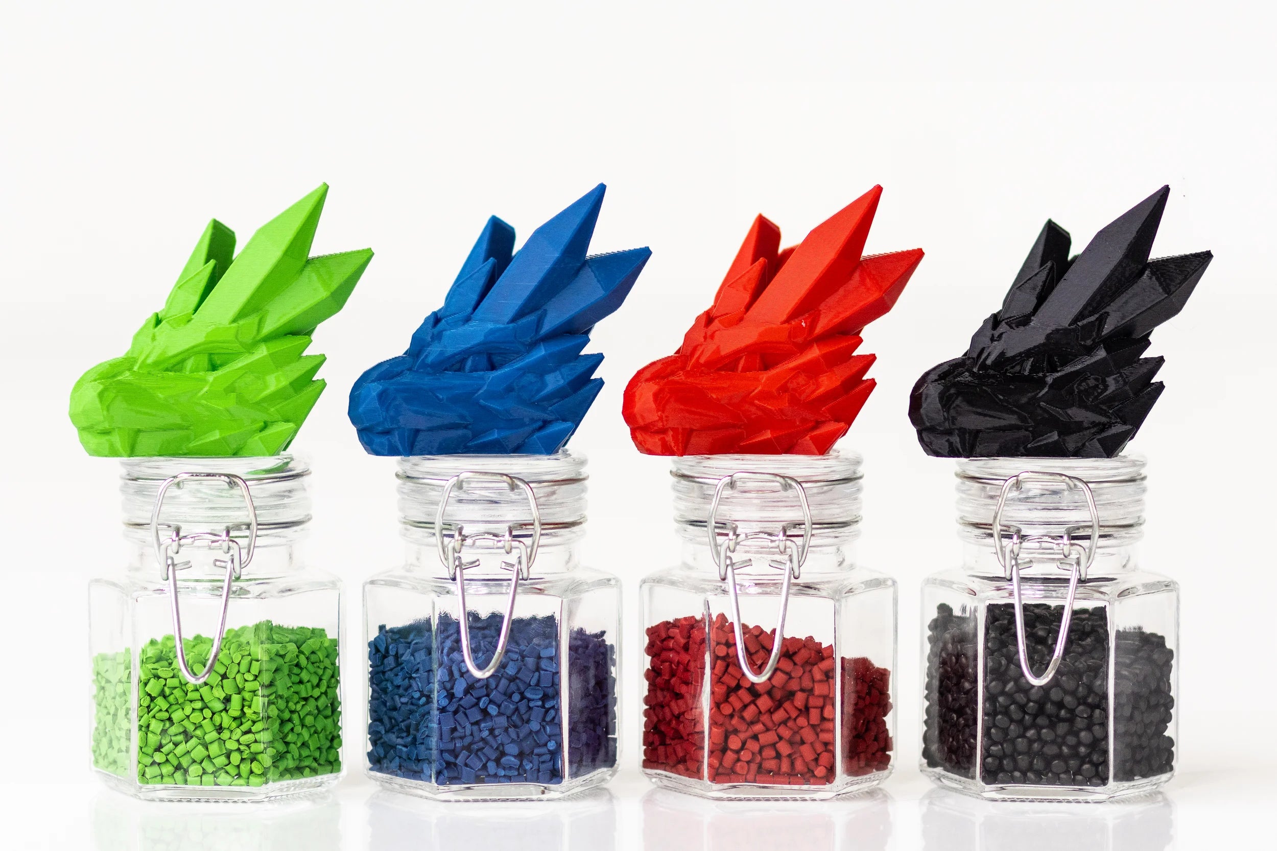 3D-printed dragon heads atop glass jars of raw filament pellets — quality materials, quality prints